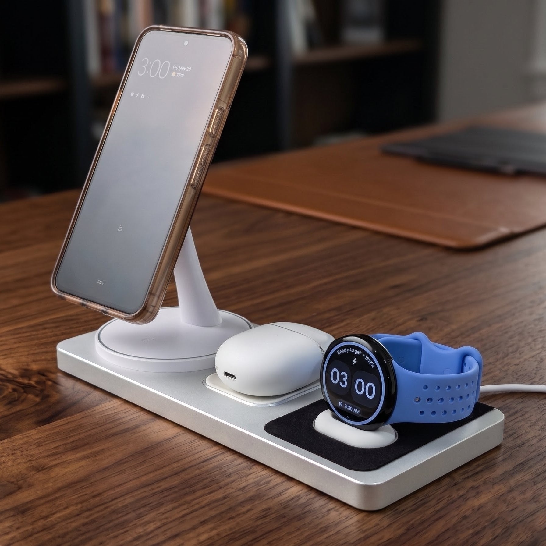 Multi-device charging station on a wooden desk with smartphone, smartwatch, and earbuds.